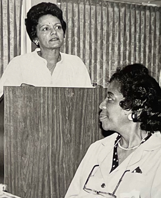 Archival photo of Urban League civic leaders at a community meeting, with a woman speaking at a podium