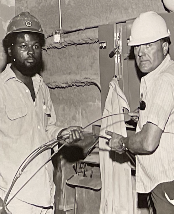 Archival photo of two workers installing electrical wiring, reflecting Urban League workforce training